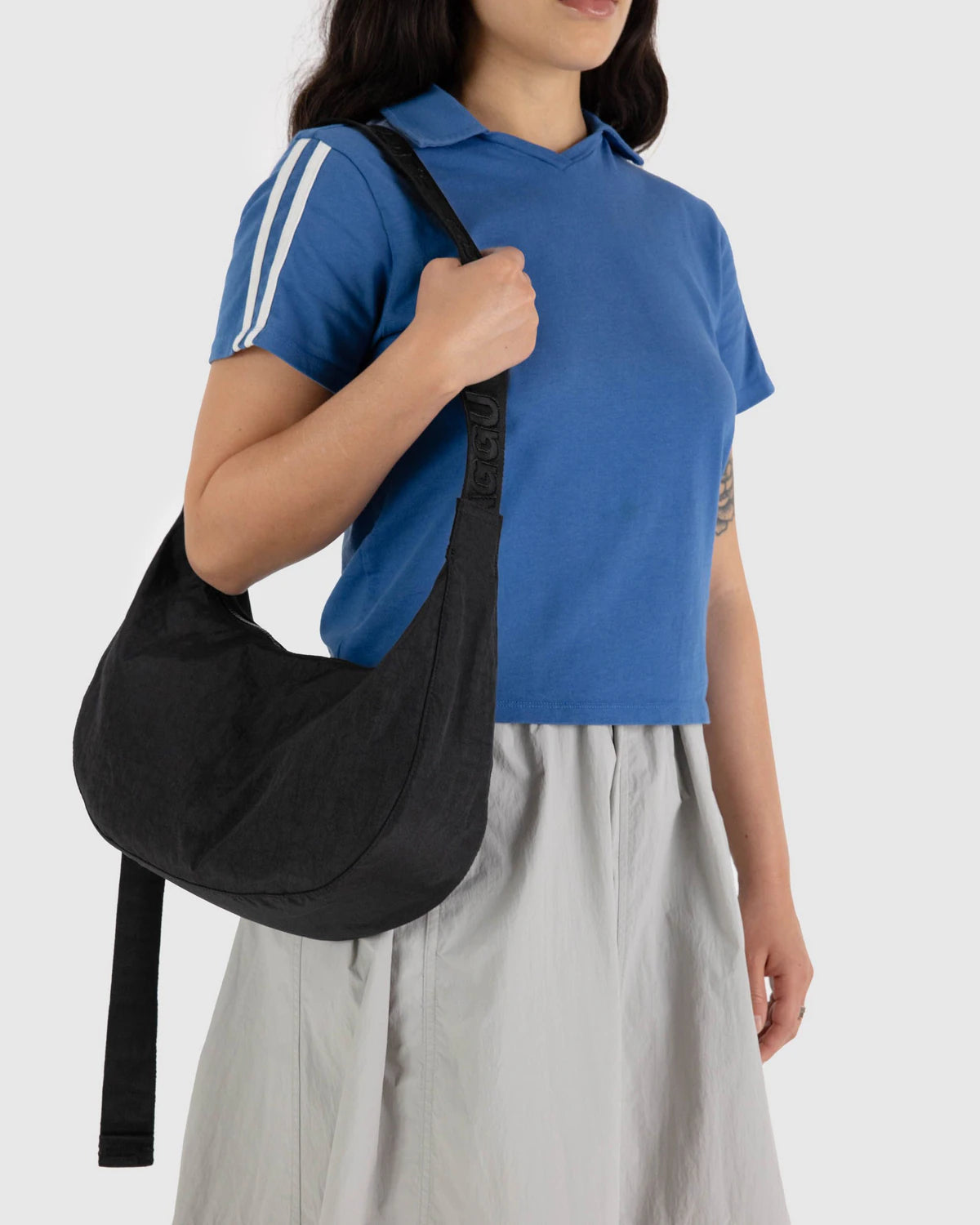 Person wearing a blue shirt with white stripes and gray pants, holding a black bag against a white background
