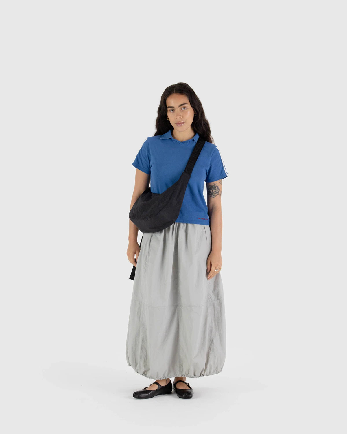 Woman wearing a blue shirt and gray skirt with a black bag on a white background