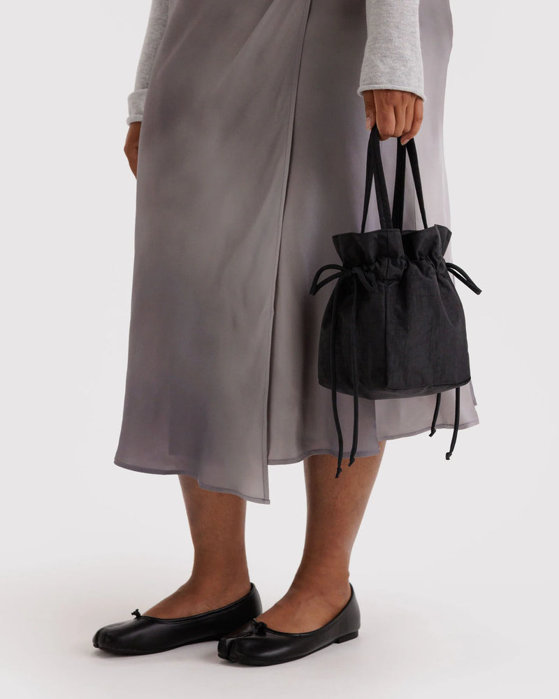 Person holding a black drawstring bag wearing a gray skirt and black shoes on a white background