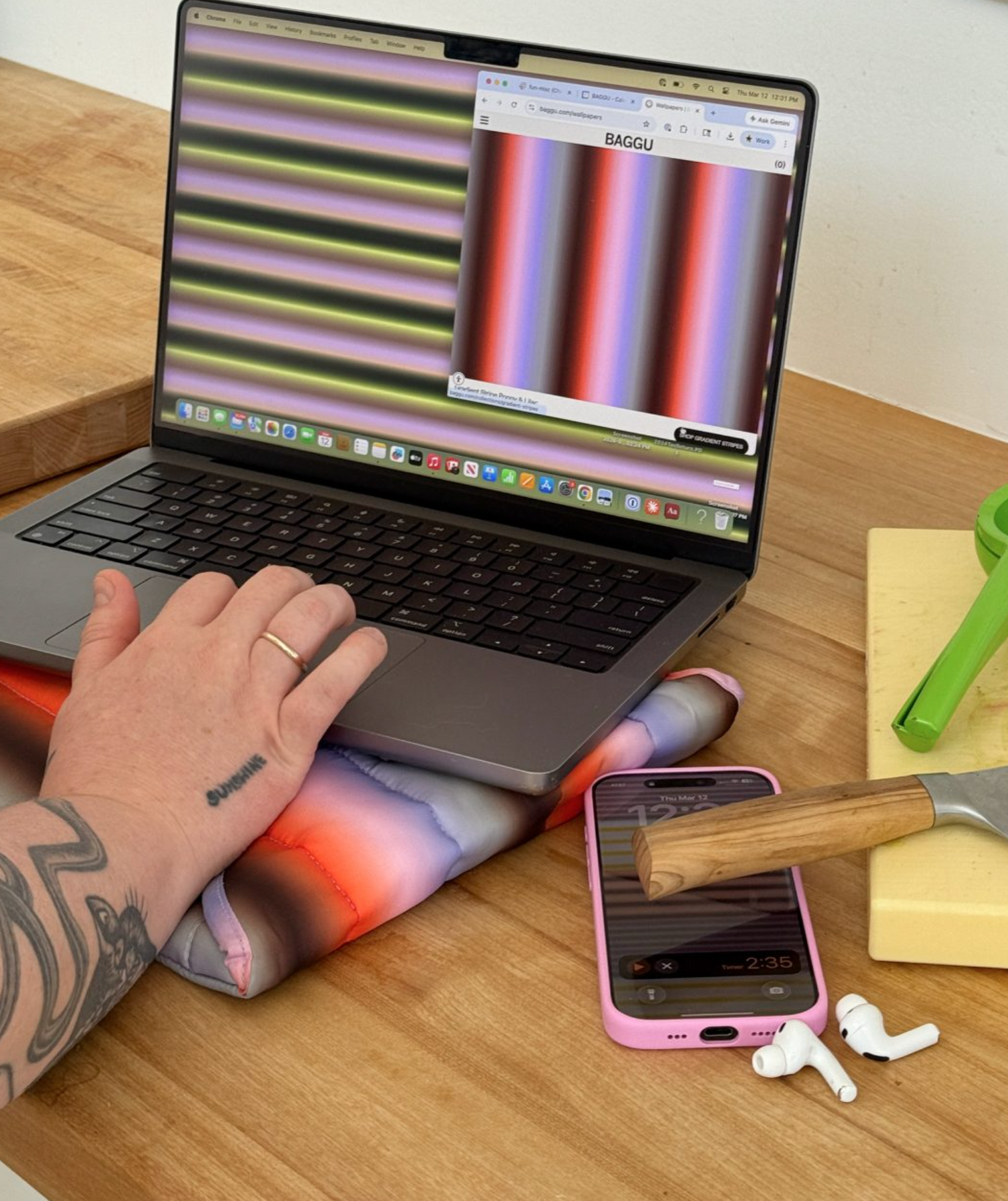 Person using a laptop on a wooden desk with a phone, hammer, and colorful towel.