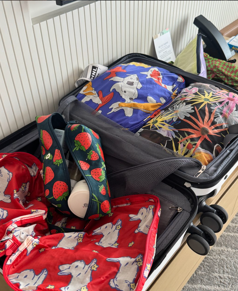 Open suitcase with colorful patterned bags on a wooden surface.