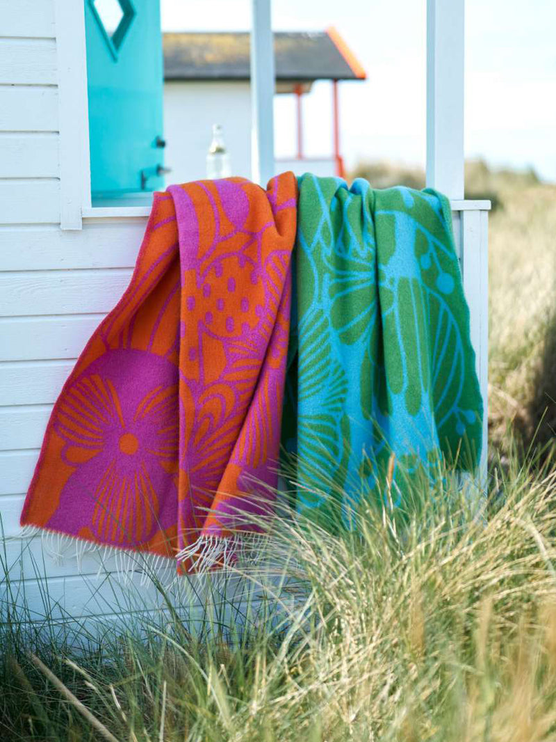 Colorful throws hanging on a white railing with a beach hut in the background.