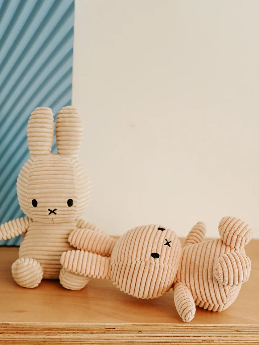 Two corduroy miffy bunnies on a wooden surface with a striped blue and white background