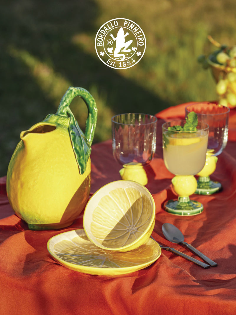 Ceramic lemon-shaped pitcher and glasses on a table with a red tablecloth, featuring Bordallo Pinheiro branding.