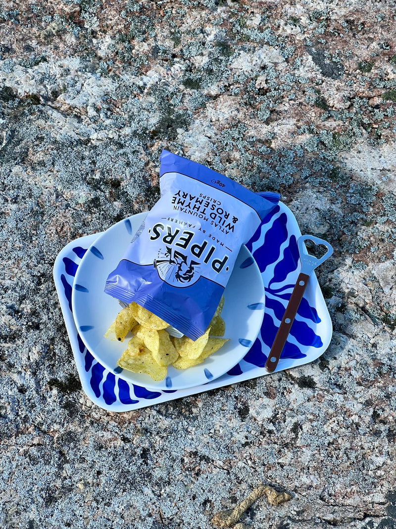Potato chips, a blue-white plate and a brown bottle opener on the tray placed on a stone surface