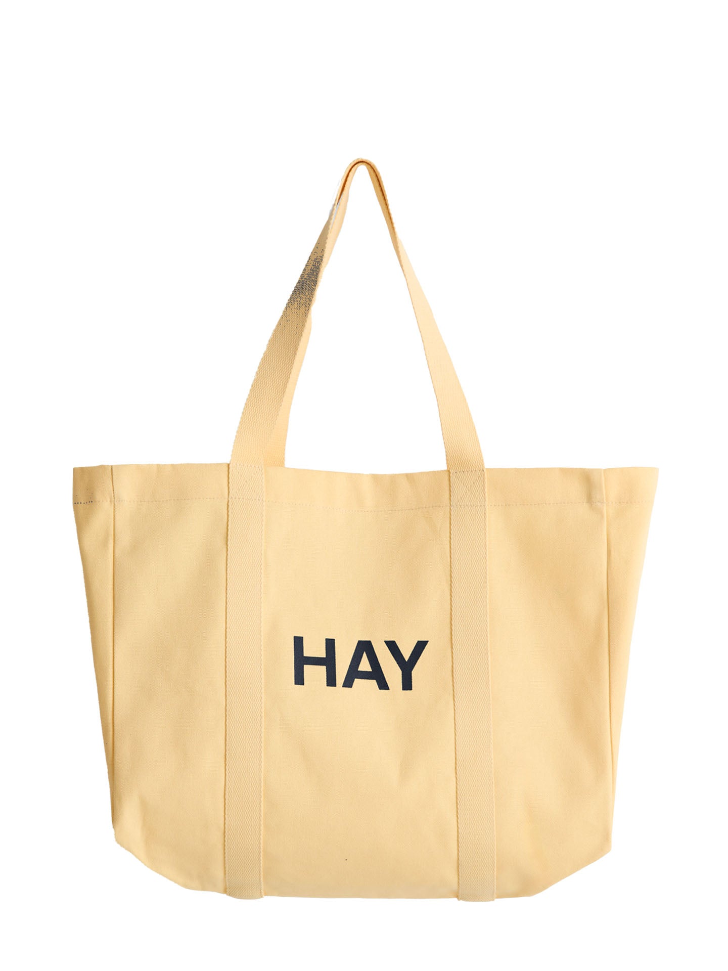 A light yellow canvas tote bag with the word 'HAY' printed in black capital letters on the front, hanging from the shoulder straps against a plain white background.