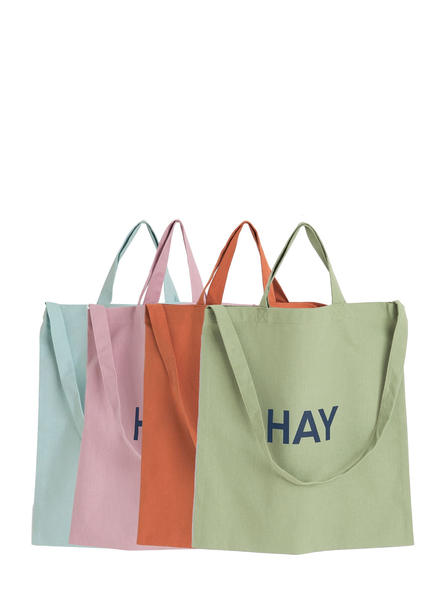 Four canvas tote bags in pastel colors (mint green, pink, orange, and sage green) arranged in a row against a white background, with the word 'HAY' printed in navy blue on the front of the rightmost bag.