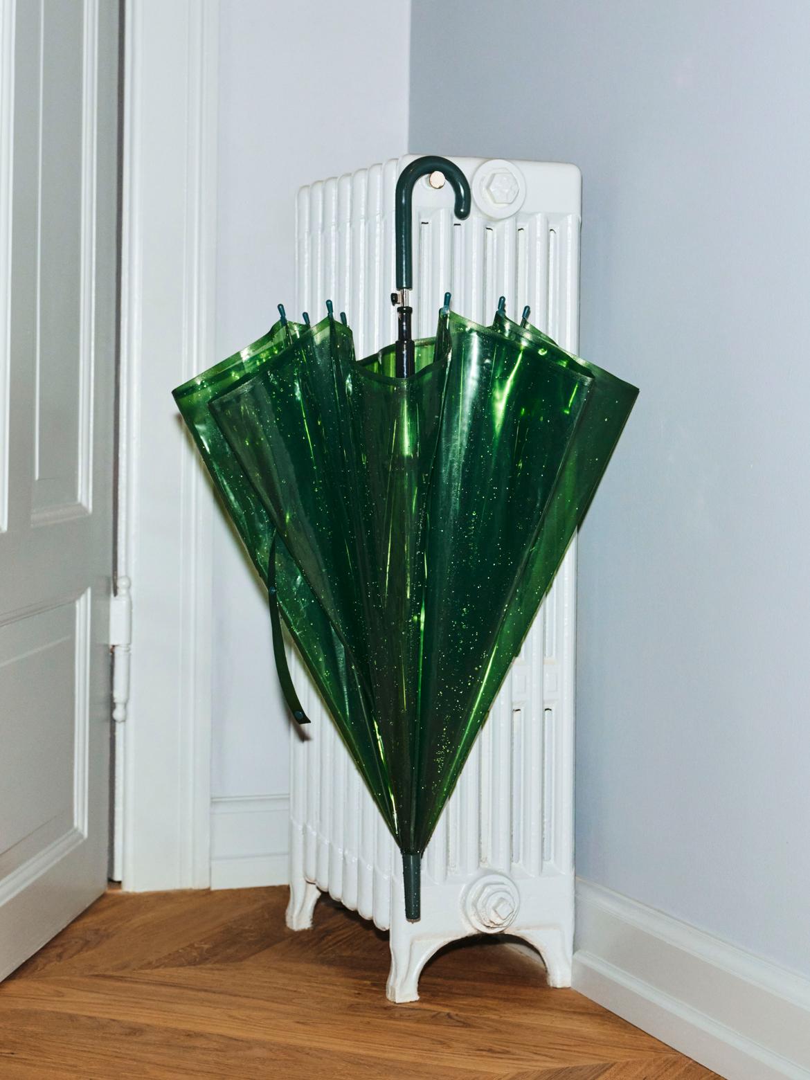 Green umbrella with a unique design standing upright against a white radiator.