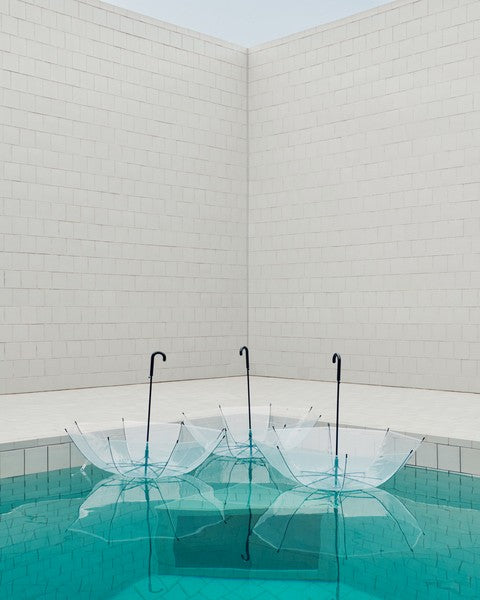 Clear umbrellas floating in a pool with white tiled walls.