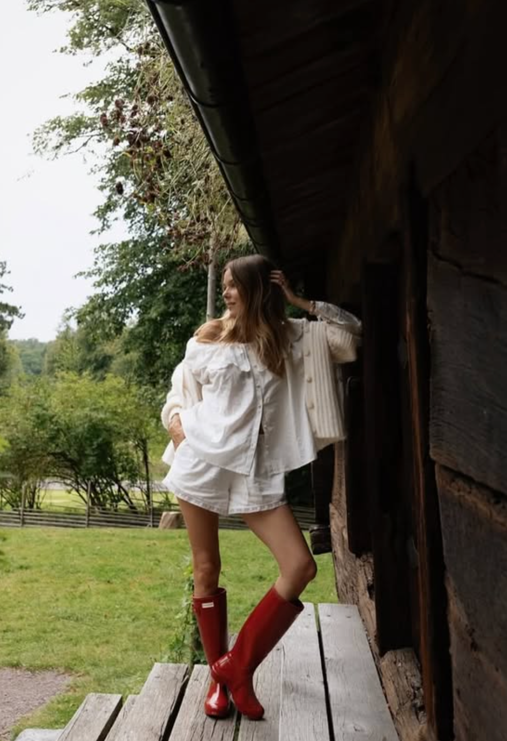 Woman in a white outfit with red boots standing on a wooden porch.