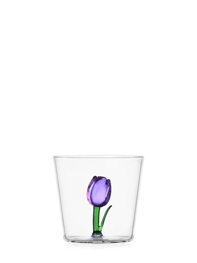 A clear glass tumbler featuring a hand-blown purple tulip with a green stem and leaves, set against a solid white background.