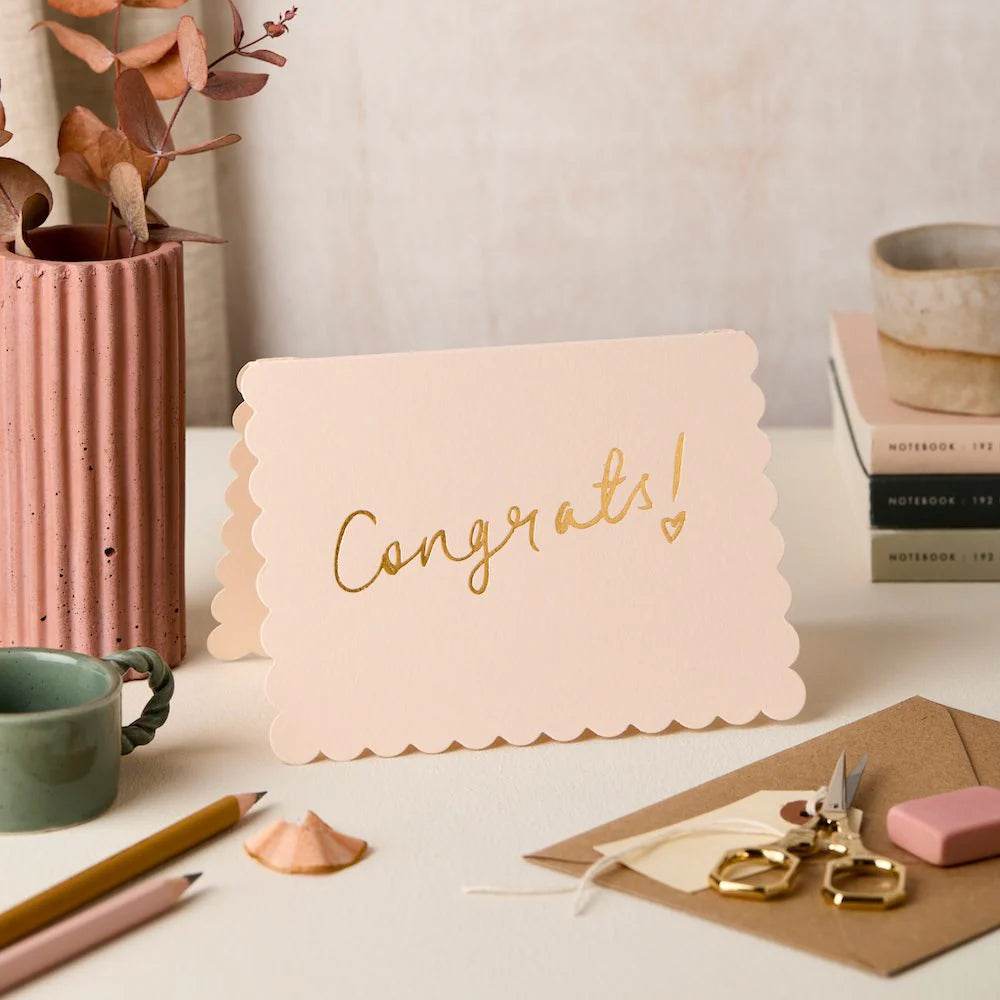 Pink card with 'Congrats!' text on a desk with stationery items