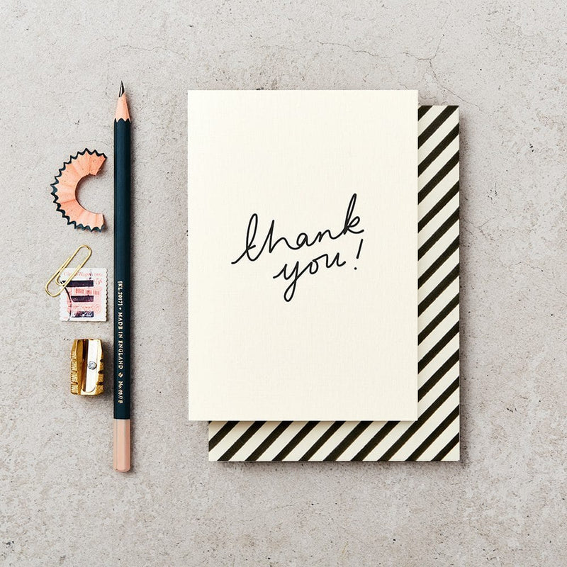 Greeting card with 'thank you!' on a gray surface with stationery items.