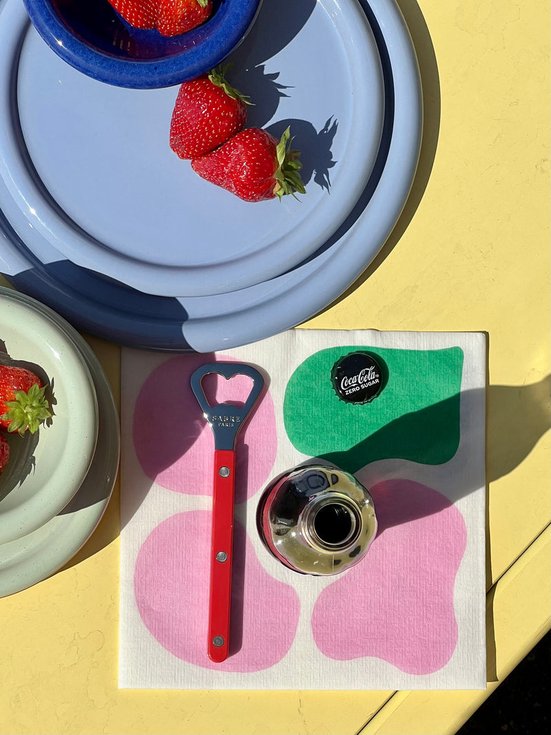 Light blue plates, paper napkin with bottle opener on a yellow surface with strawberries.