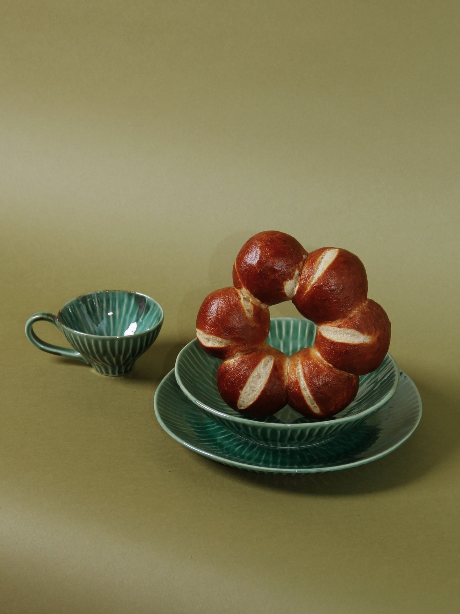 Teal ceramic cup and saucer with a ring-shaped bread on a matching plate against a beige background