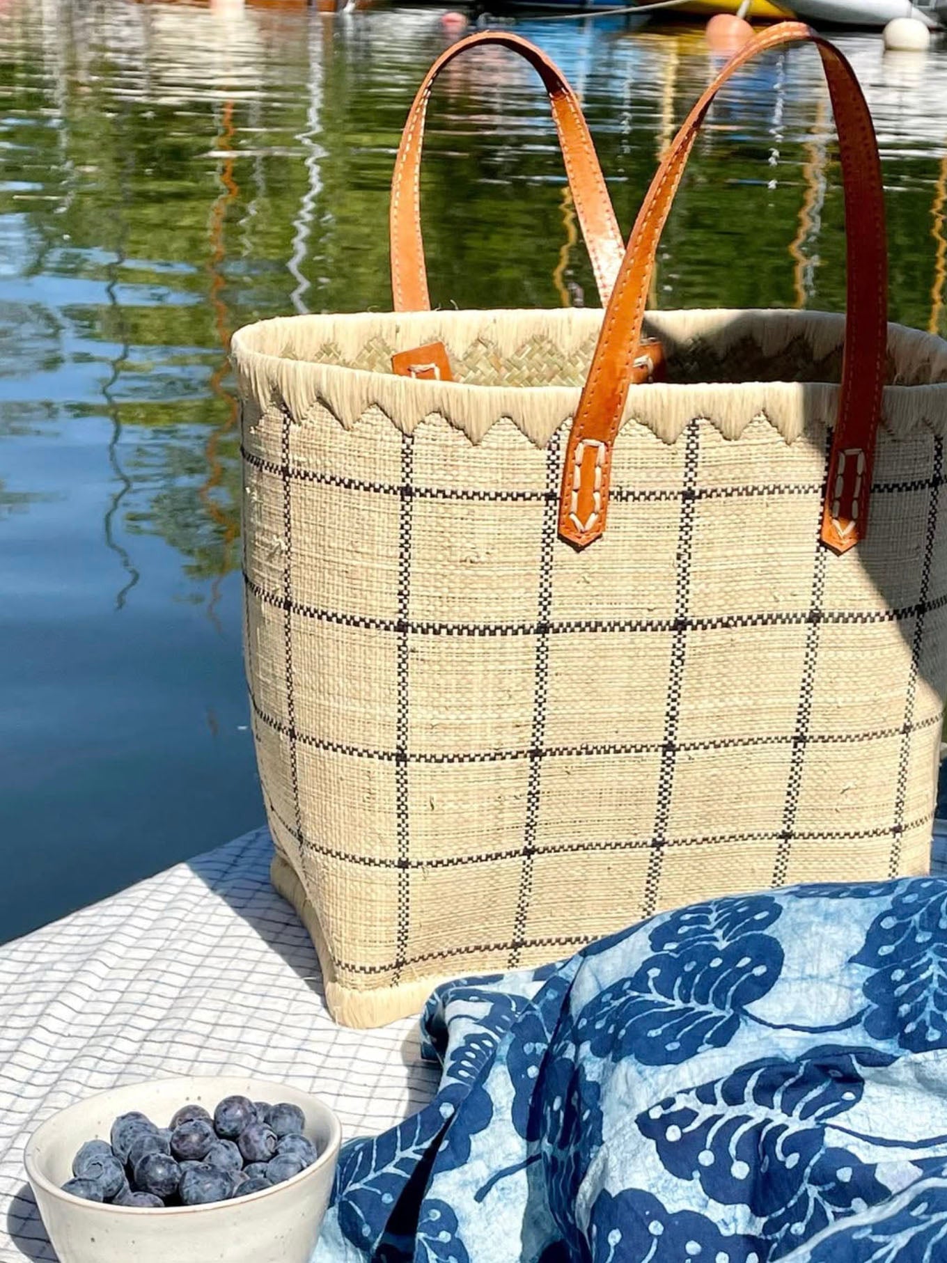 Plaid raffia tote bag with leather handles on a dock by water