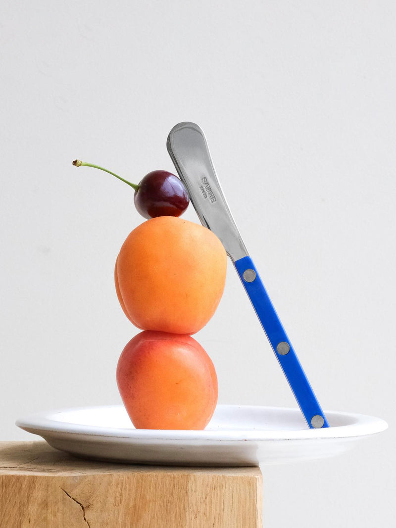 Two apricots stacked on a plate with a knife leaning against them, on a light wooden surface.