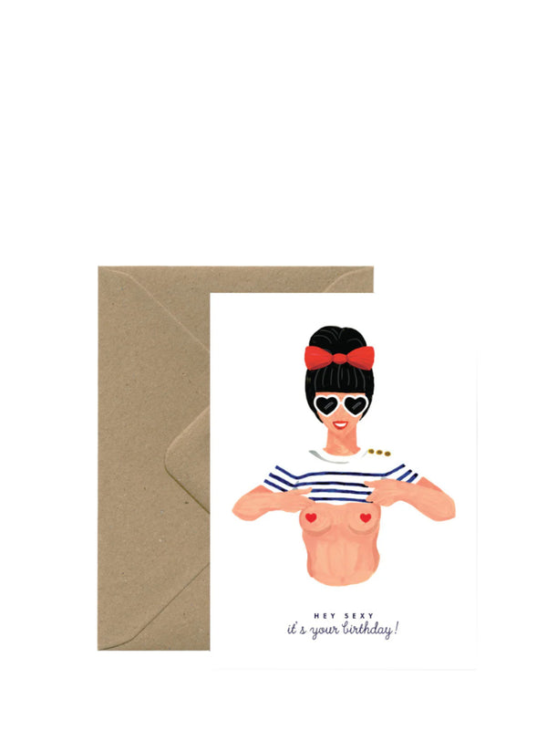 A birthday card with an illustration of a woman wearing sunglasses and a striped top, with a text that reads 'Happy Birthday! Now you're old!' The card is accompanied by a brown envelope.