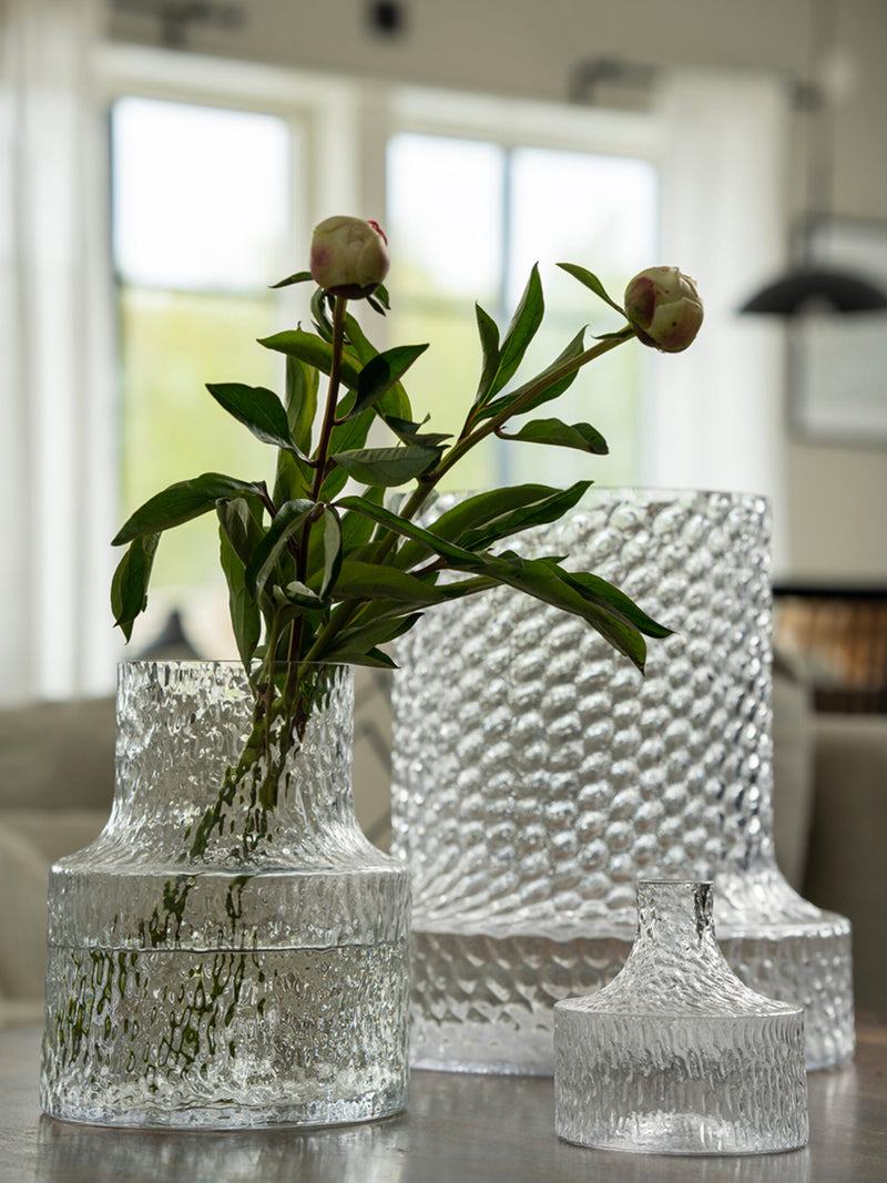 Clear textured glass vases with a plant on a reflective surface