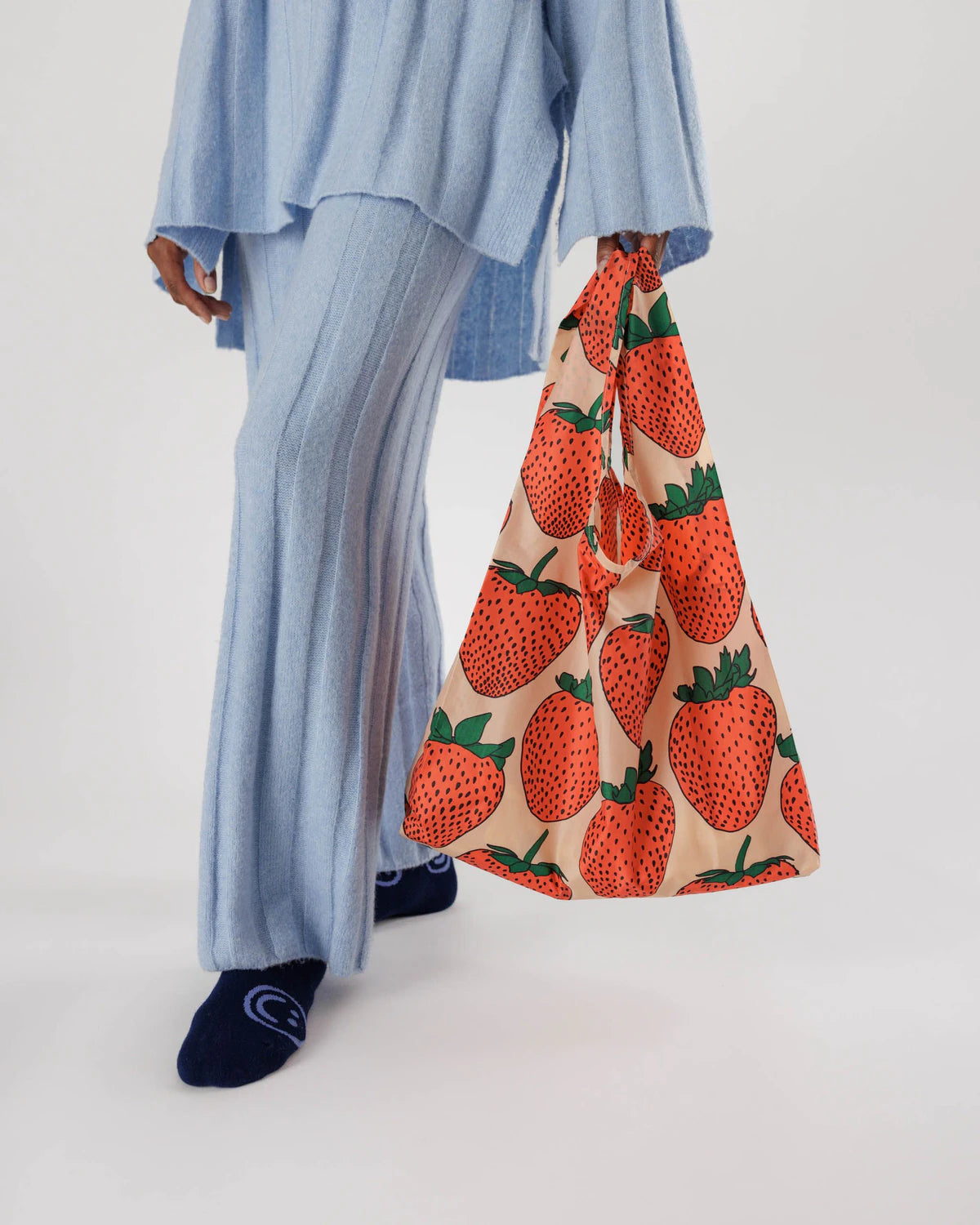 Person wearing a blue outfit with a strawberry-patterned bag on a white background