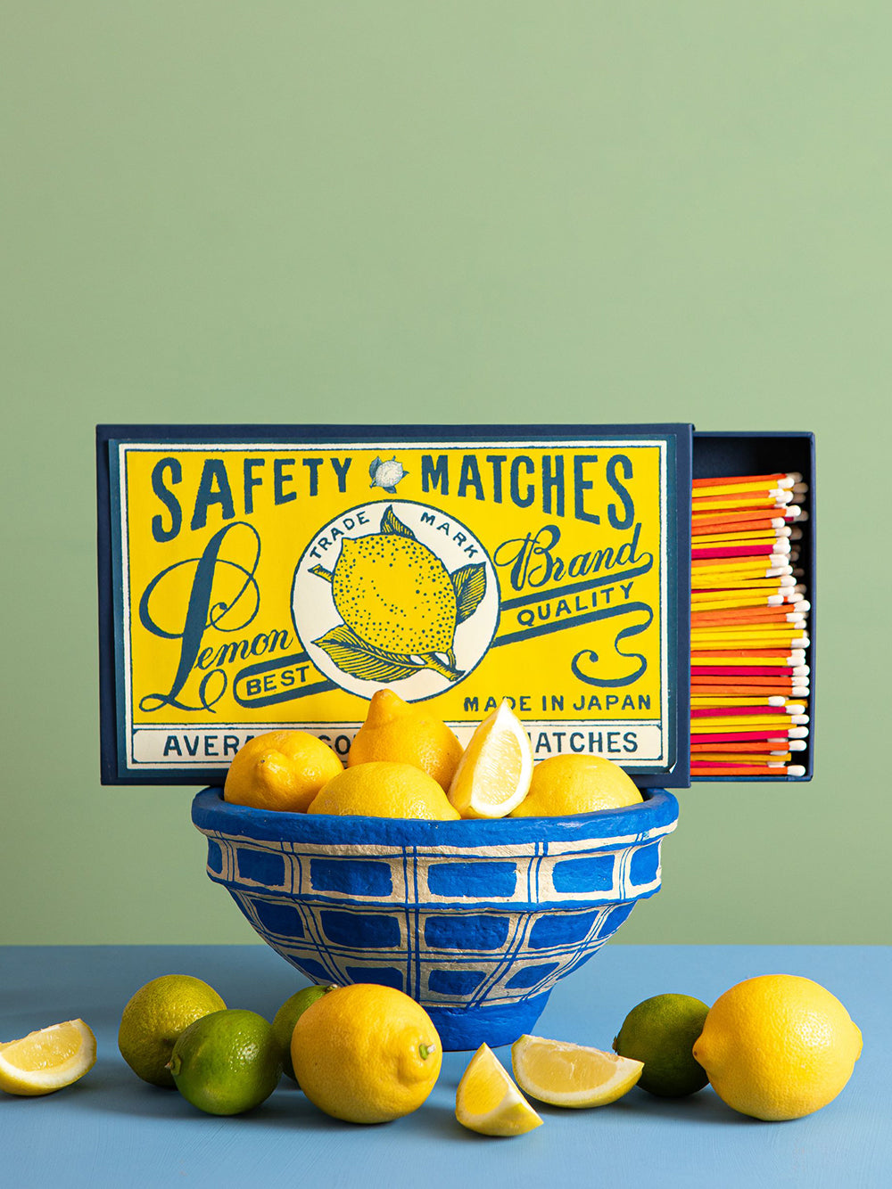 Giant vintage-style safety matches box with lemons around a blue bowl on a green and blue background