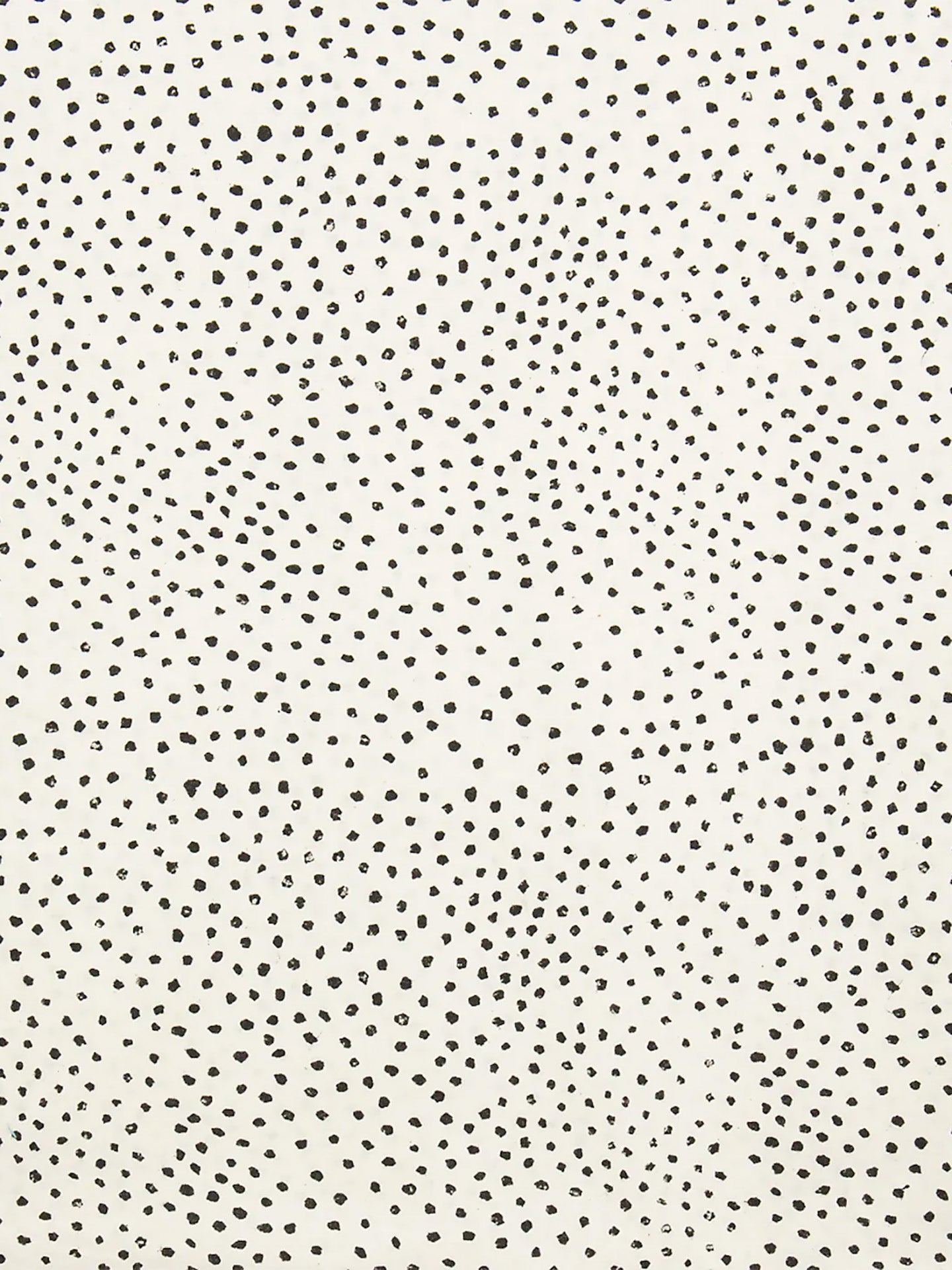 A close-up of thin soft cotton fabric with a warm off-white background covered in small, irregular black speckles and dots.
