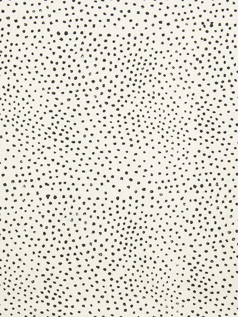 A close-up of thin soft cotton fabric with a warm off-white background covered in small, irregular black speckles and dots.