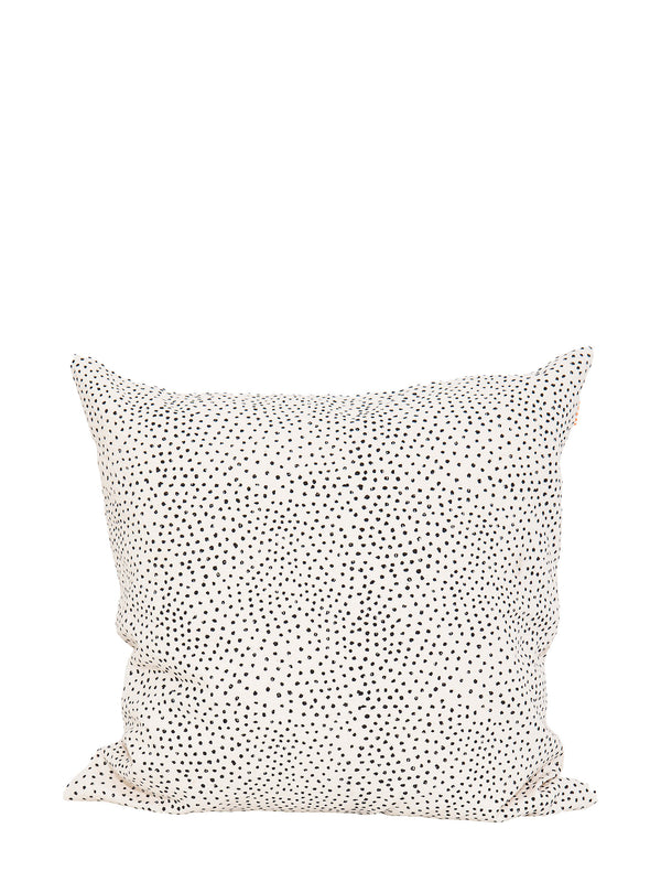 A square cushion made from off-white cotton with black hand-printed flecks or irregular little dots suitable for home decoration such as couches, settees, sofas and armchairs, standing against a white background.