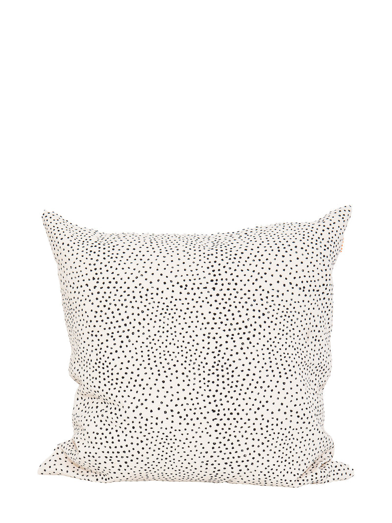A square cushion made from off-white cotton with black hand-printed flecks or irregular little dots suitable for home decoration such as couches, settees, sofas and armchairs, standing against a white background.