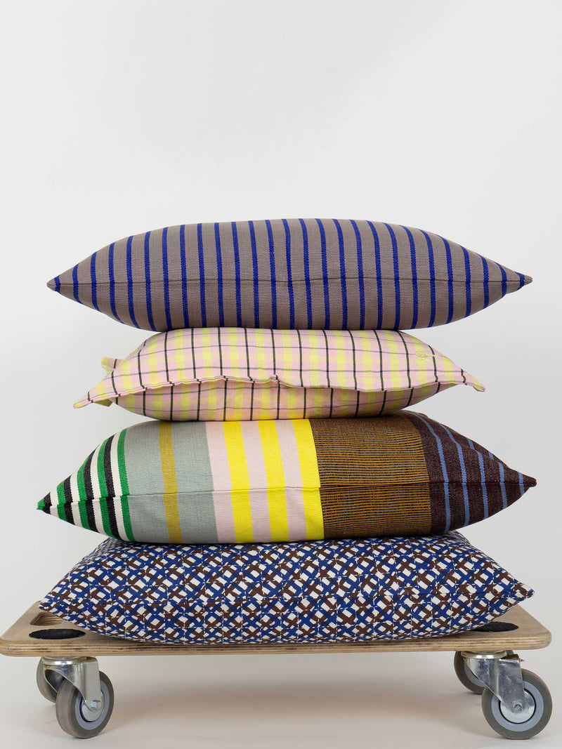 Stack of colorful patterned pillows on a wooden cart with wheels against a white background