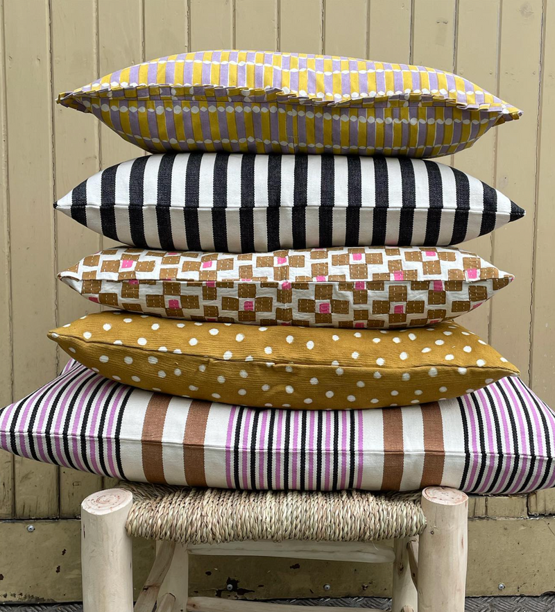 Stack of colorful patterned cushions on a wooden stool against a wooden wall.