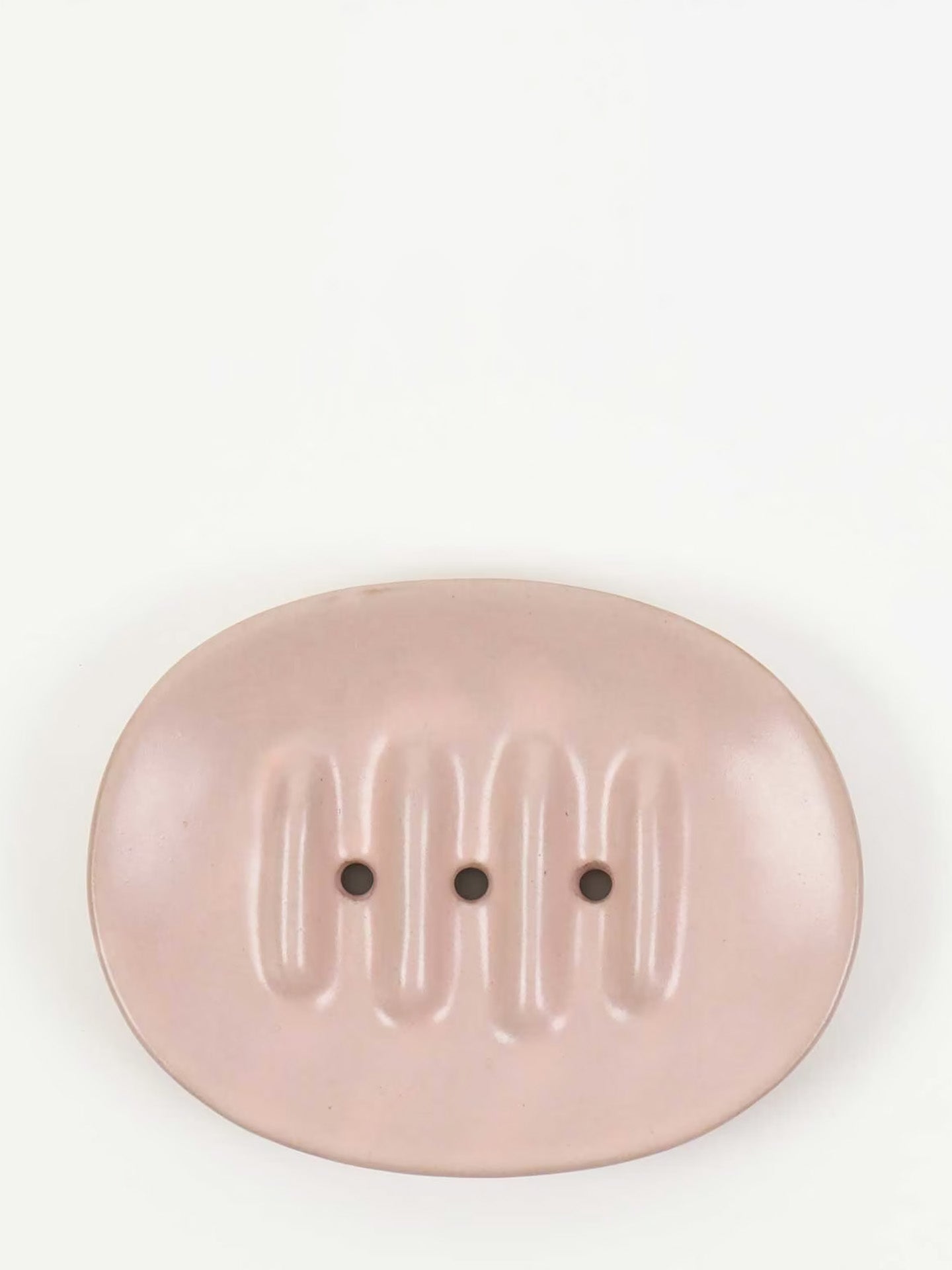 An oval-shaped, light pink ceramic soap dish with three vertical grooves and three small drainage holes, set against a plain white background.
