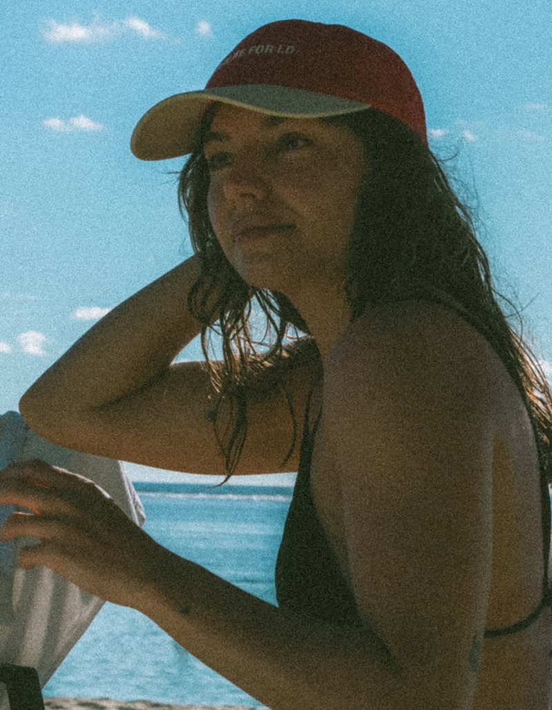 Person wearing a red cap with text, standing by a body of water.