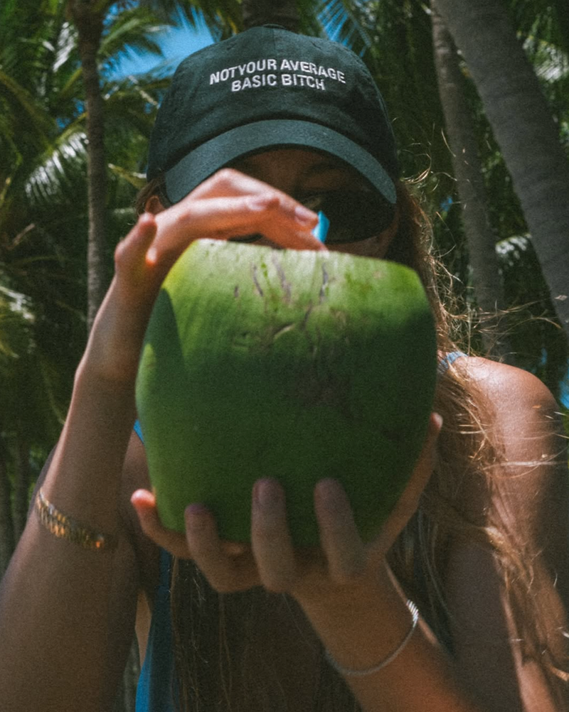 Person holding a green coconut with a cap in a tropical setting