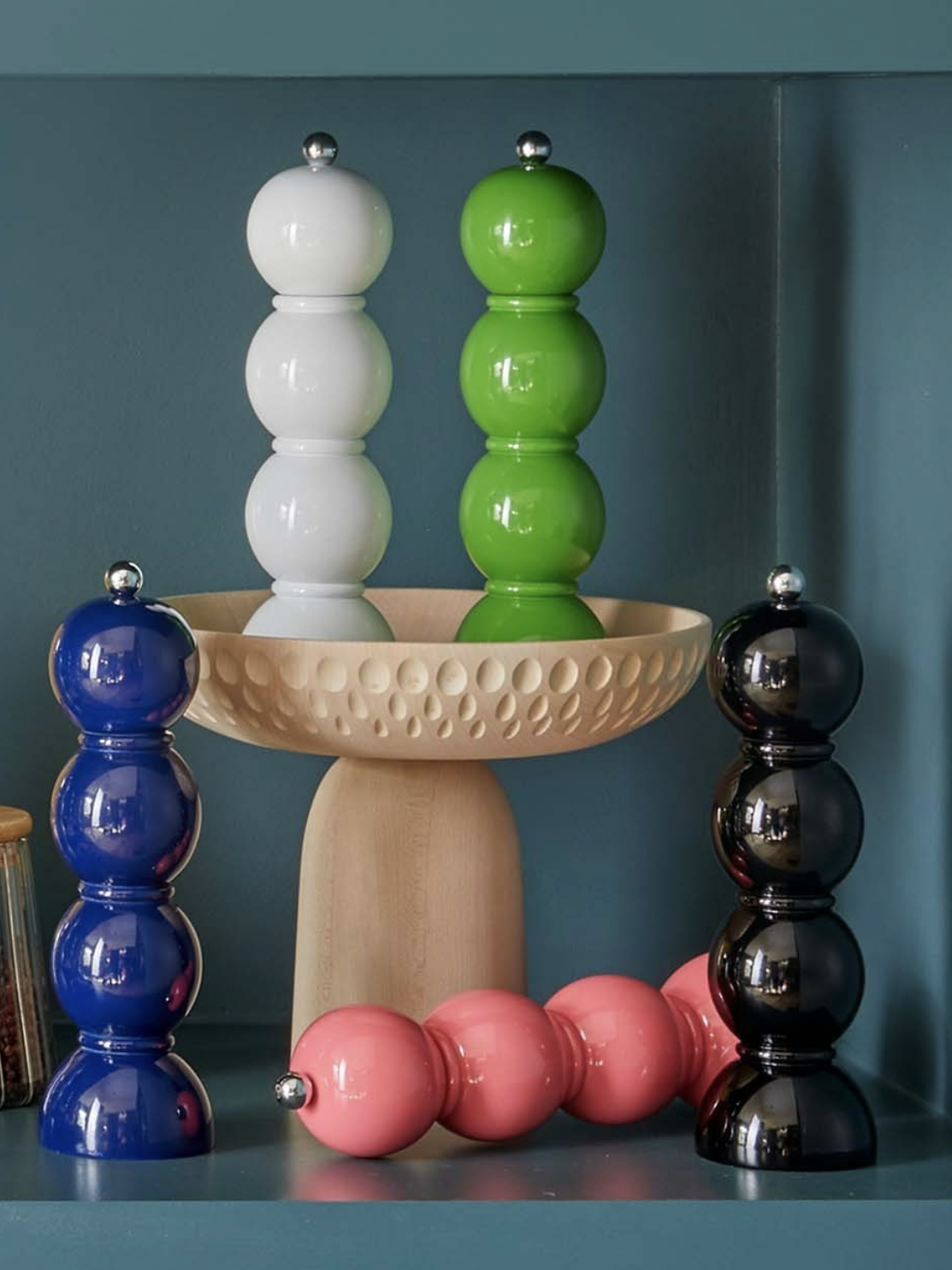 Colorful salt and pepper shakers on a wooden stand against a blue wall.