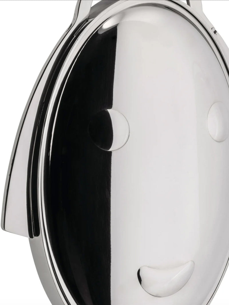 A close-up of a closed polished silver metal cake stand folding, featuring a a streamlined face with a smile and bab haircut, on a smooth reflective surface with circular and curved details against a white background.