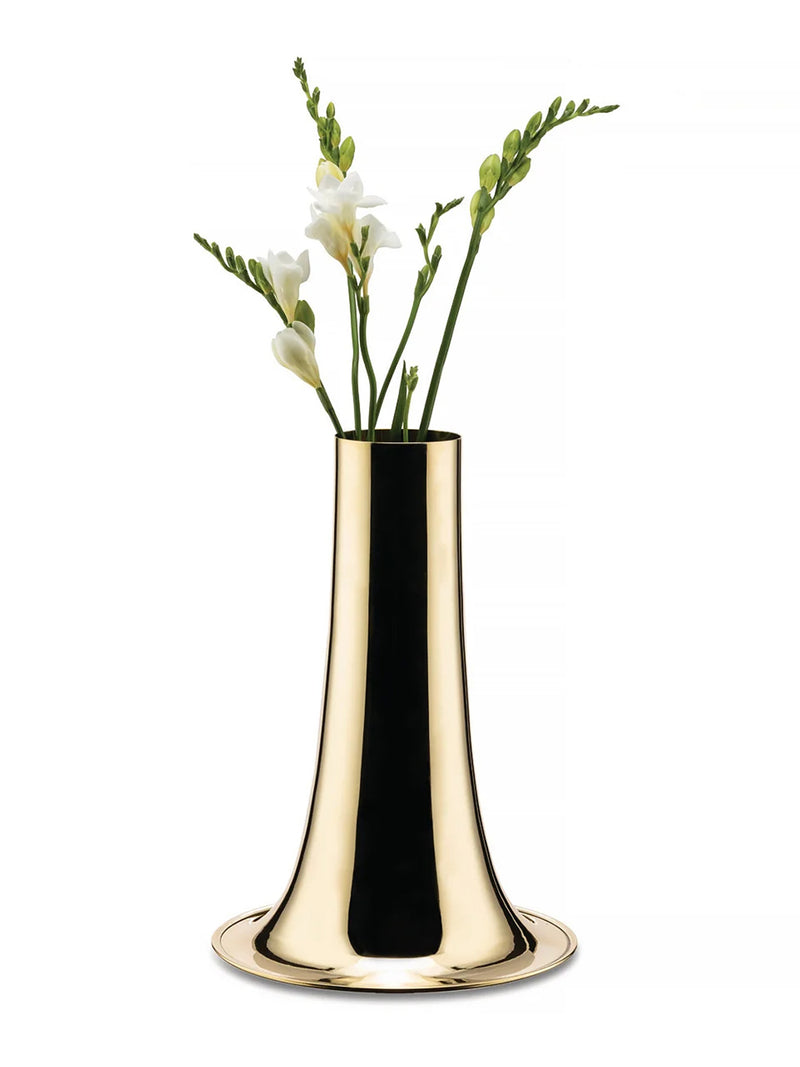A polished gold metal vase with a flared bell-shaped body and circular base, holding white flowers with green stems, set against a plain white background.
