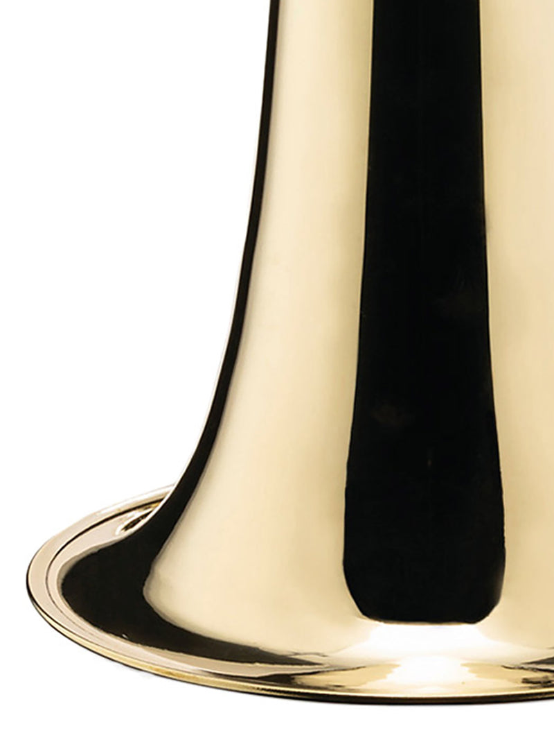 Close-up of the base of a polished brass bell-shaped vase, showing a reflective gold surface with a dark vertical reflection on a white background.