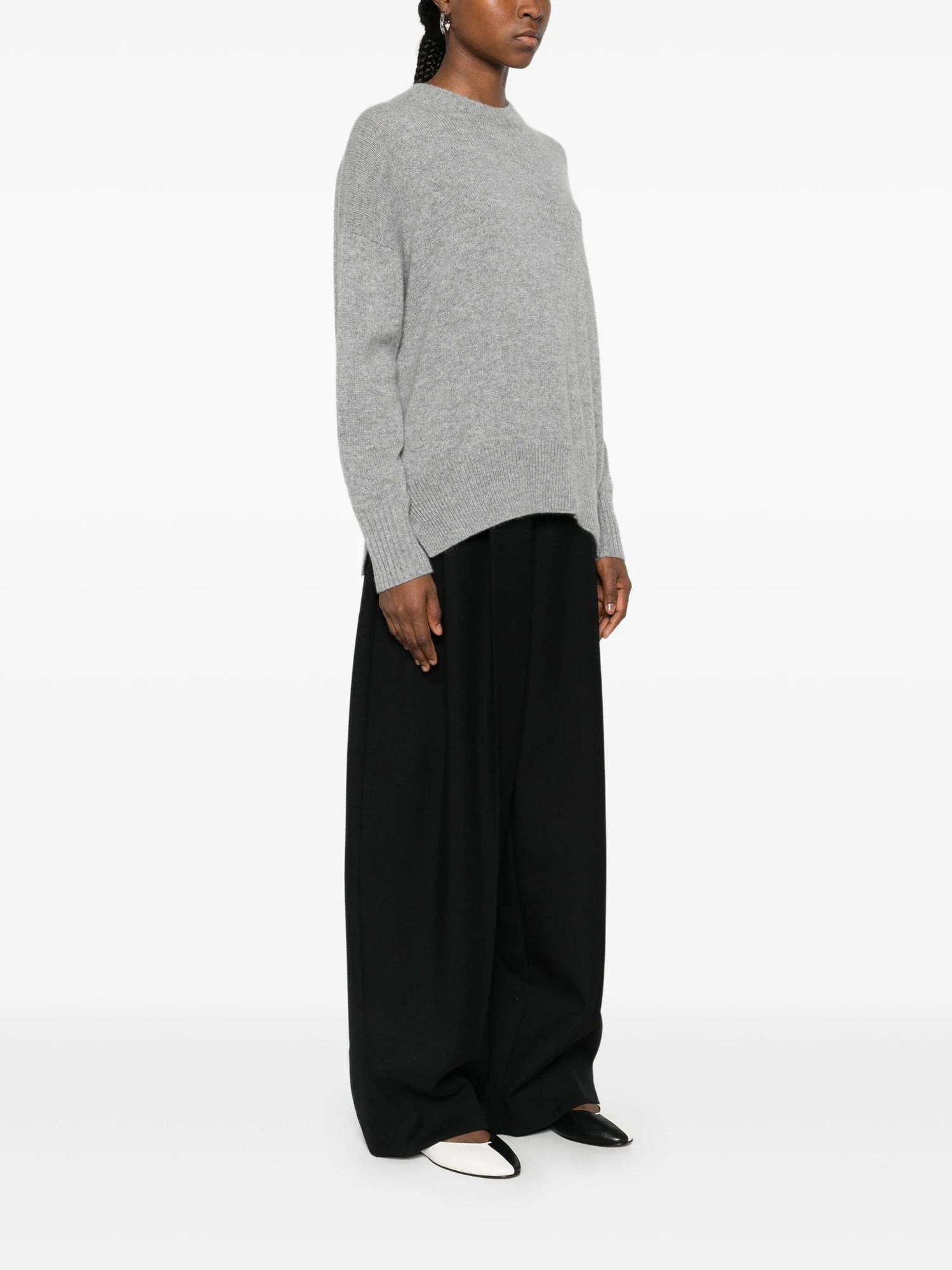 Person wearing a gray sweater and black pants on a white background