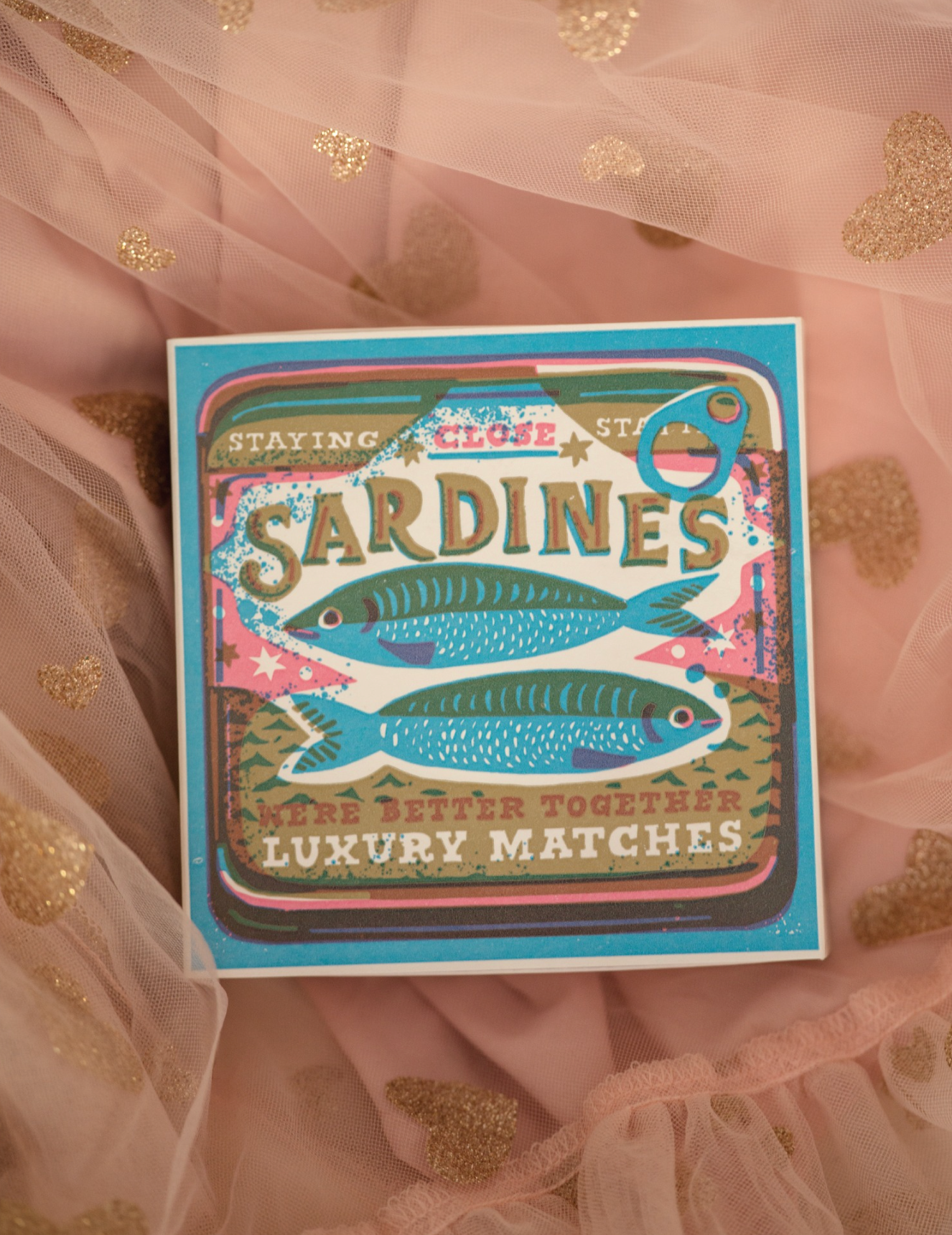 Matchbox labeled 'Sardines' on a sheer fabric background with gold dots