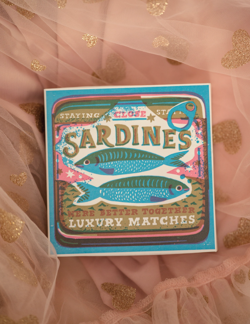Matchbox labeled 'Sardines' on a sheer fabric background with gold dots