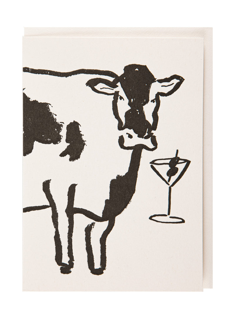 A double greeting card with a minimalist black ink illustration of a cow and a martini glass on an off-white background, shown with an envelope behind it.