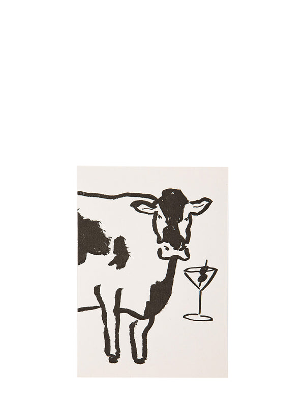 A minimalist illustrated greeting card featuring a black-and-white cow and a martini glass on a warm off-white background, shown against a solid white backdrop.
