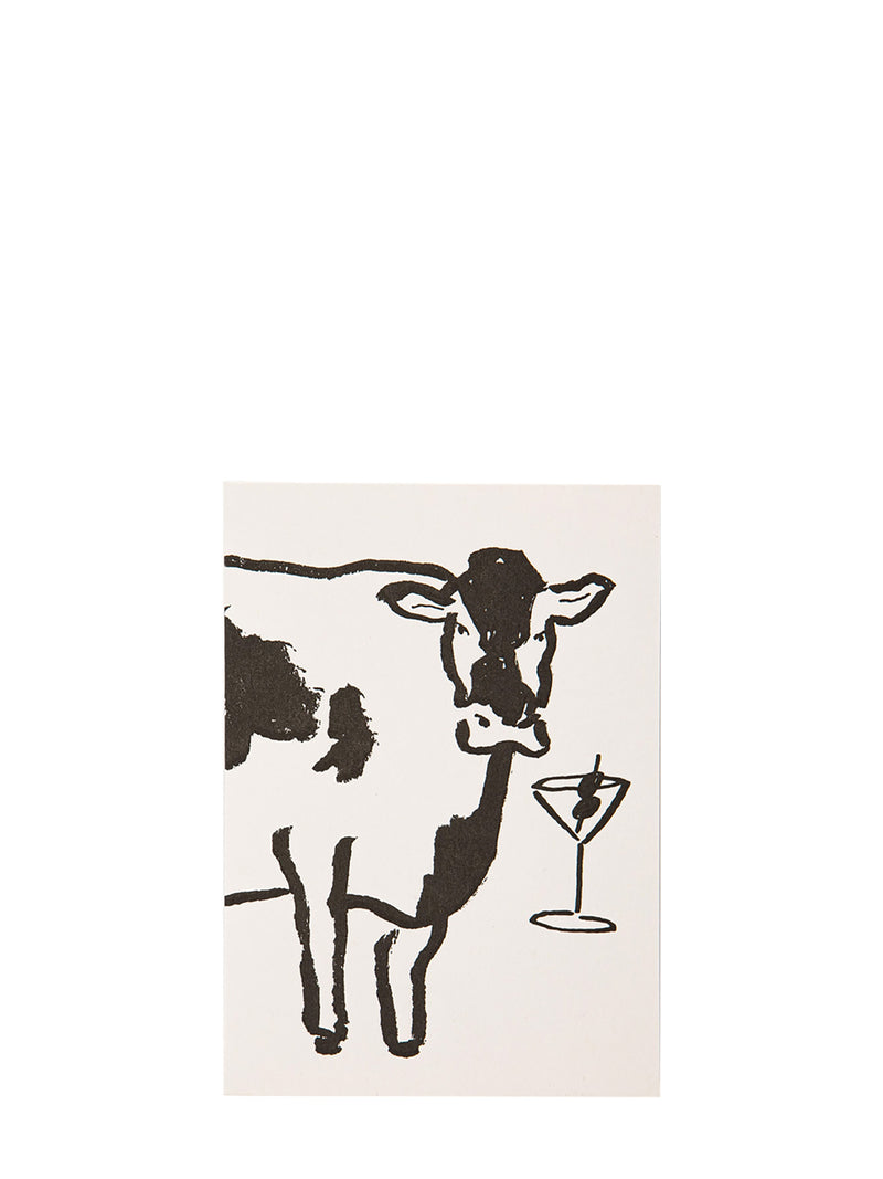A minimalist illustrated greeting card featuring a black-and-white cow and a martini glass on a warm off-white background, shown against a solid white backdrop.