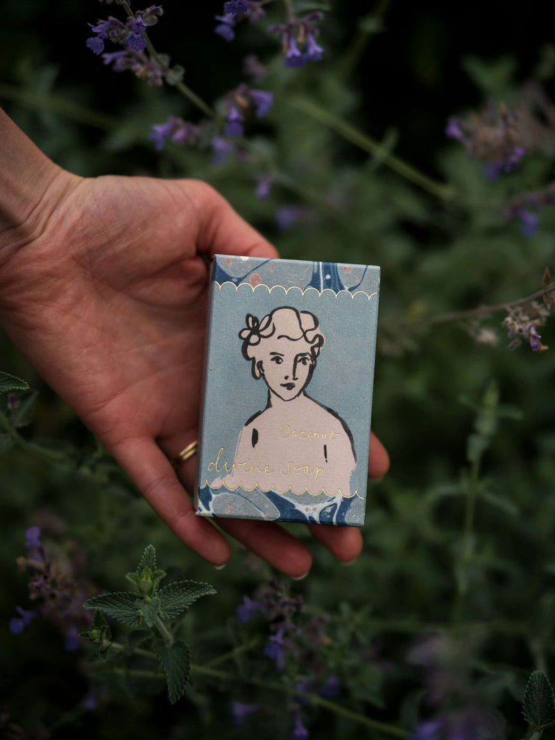 Hand holding a small decorative box with a face design against a natural background
