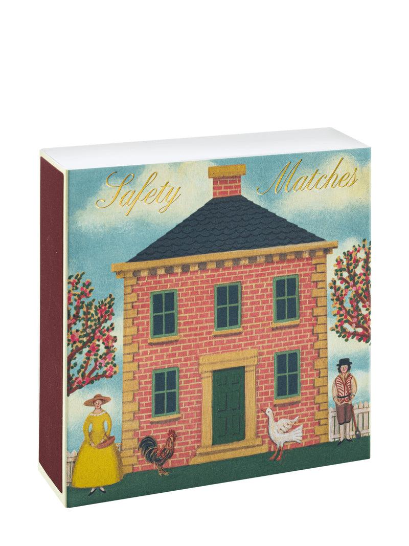 A vintage-style matchbox package labeled 'Safety Matches' with an illustration of a brick house, trees, a woman in a yellow dress, a rooster, and a goose. The package is photographed on a plain white background.