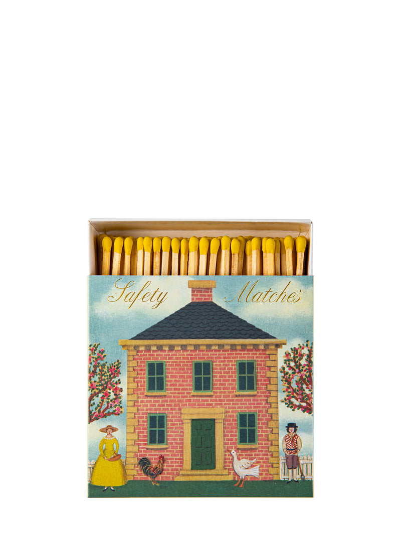 An open box of vintage-style safety matches with a illustrated cover showing a Queen Anne style brick house between to flowering trees and a woman and a man, with some farm animals, photographed on a plain white background.