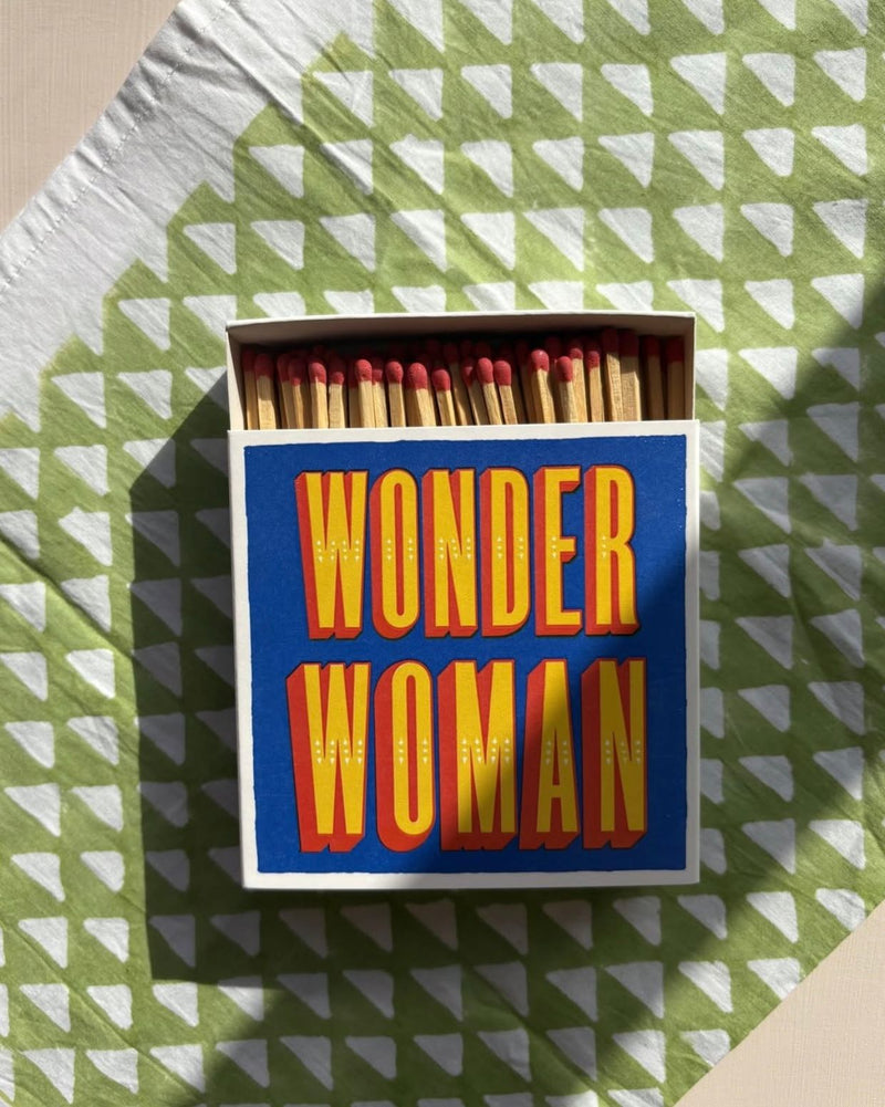 Matchbox with 'Wonder Woman' text on a green and white patterned surface
