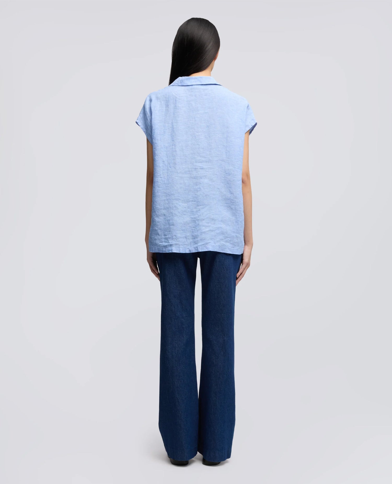 Person wearing a light blue sleeveless linen top and dark blue pants on a gray background