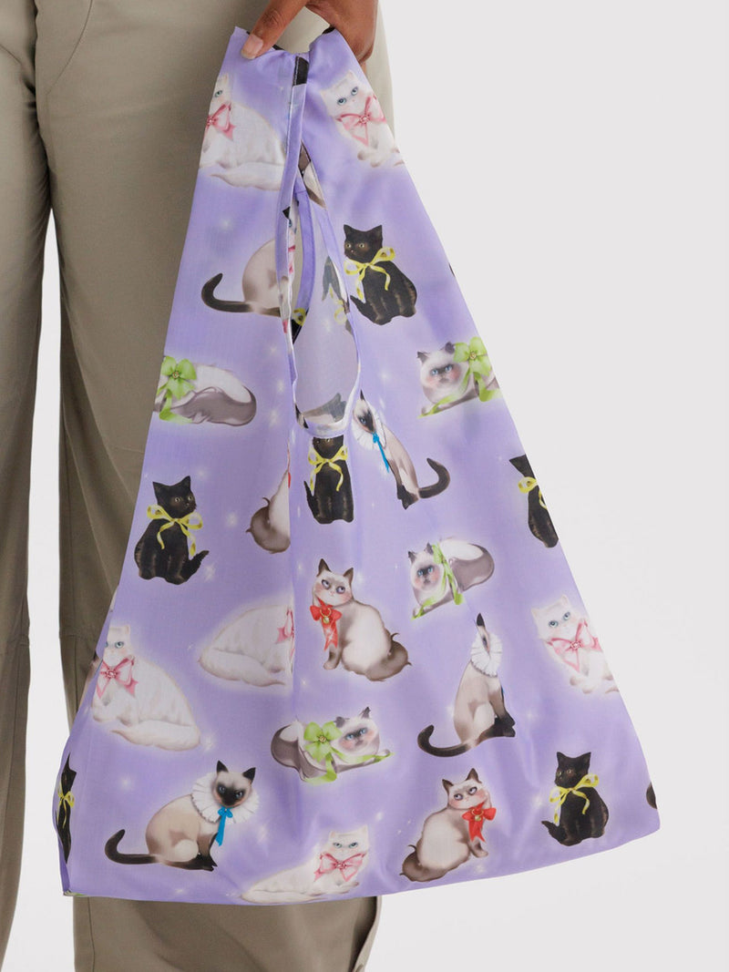 Purple reusable bag with cat pattern held by a person wearing beige pants.
